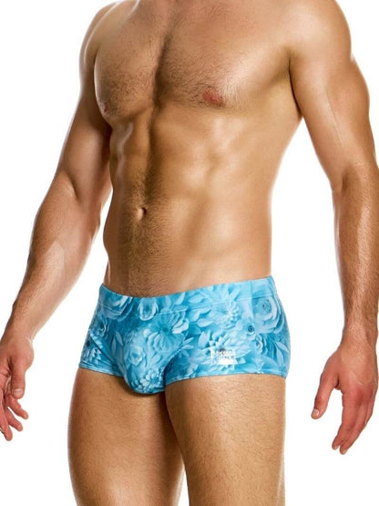 Man wearing blue swim briefs with a floral pattern on a white background