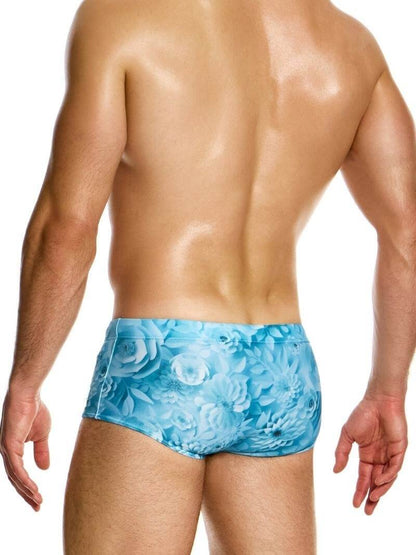 Man wearing blue swim briefs with floral pattern on a white background