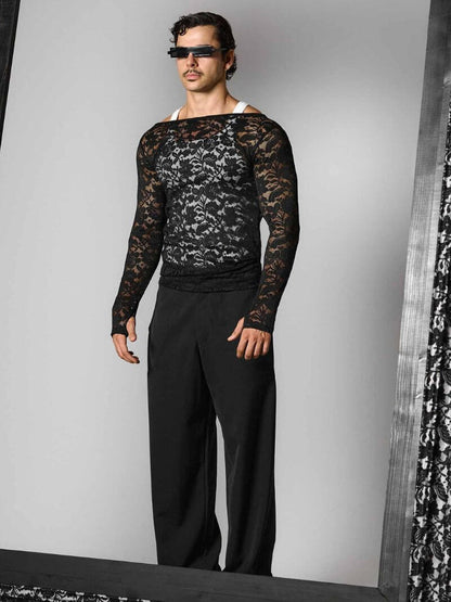 Person wearing a black lace long-sleeve top and black pants against a gray background