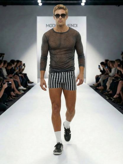 Model walking on a fashion runway wearing a sheer top and striped shorts.