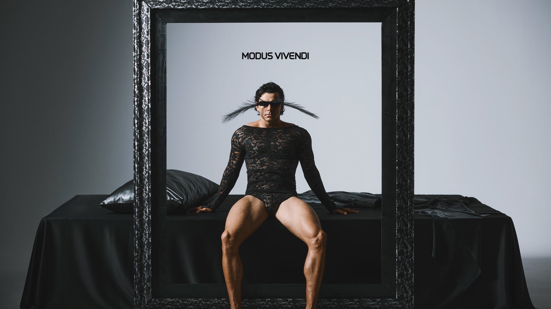 Person wearing a black lace outfit sitting inside a framed picture with 'Modus Vivendi' branding.