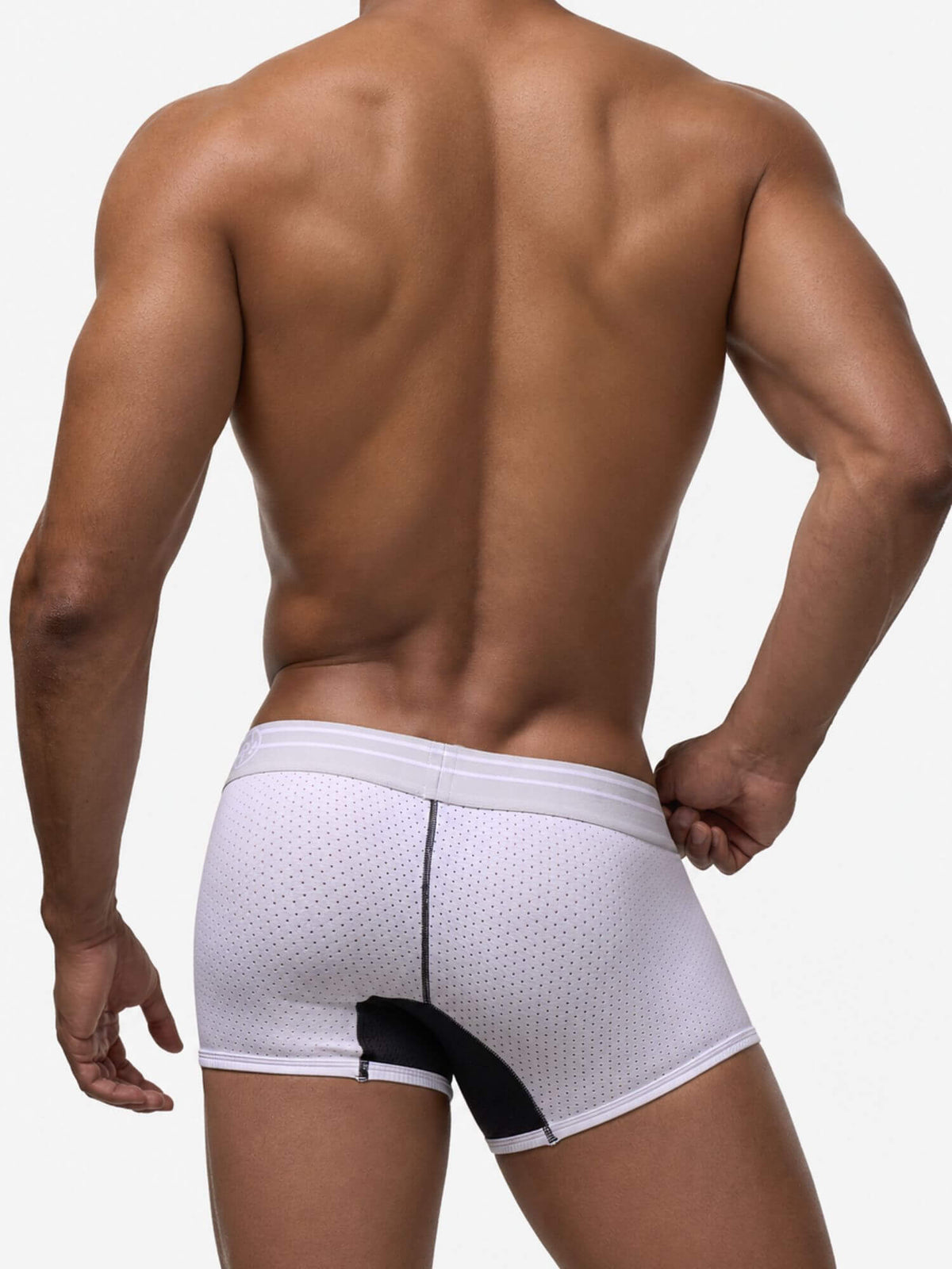 Rear view of a muscular man wearing white mesh boxer briefs with a black side panel and white waistband, against a light gray studio background.