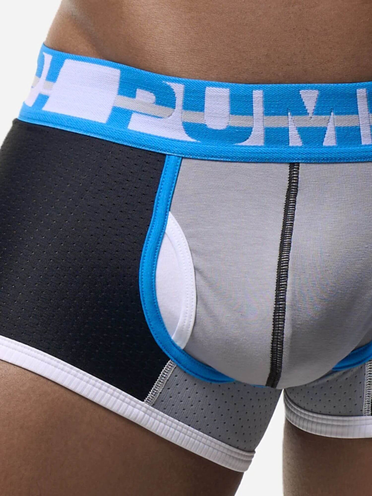 Close-up of a person wearing men's boxer briefs with a black perforated side panel, light gray front panel, white leg opening trim, and a bright blue waistband with a white logo.