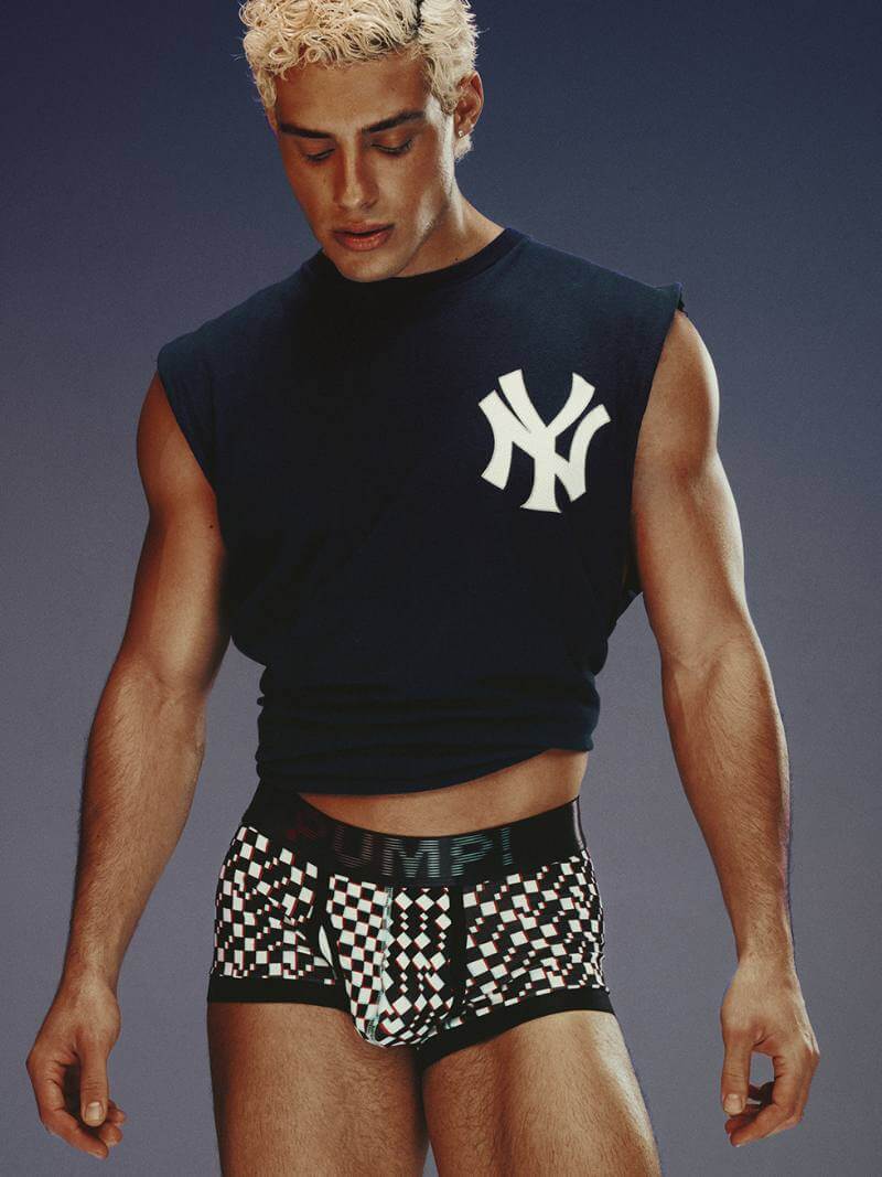 Person wearing a black sleeveless shirt with a logo and checkered boxer briefs on a gray background
