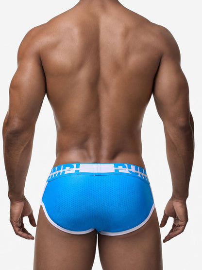 Rear view of a muscular man wearing bright blue athletic briefs with a white waistband and white trim, against a light gray studio background.