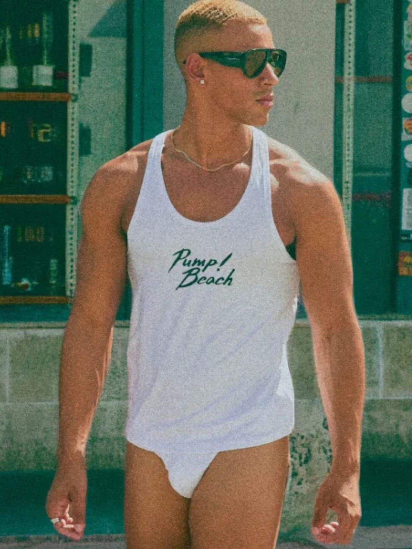 Man wearing a white tank top with 'Pump Beach' text in a casual setting.
