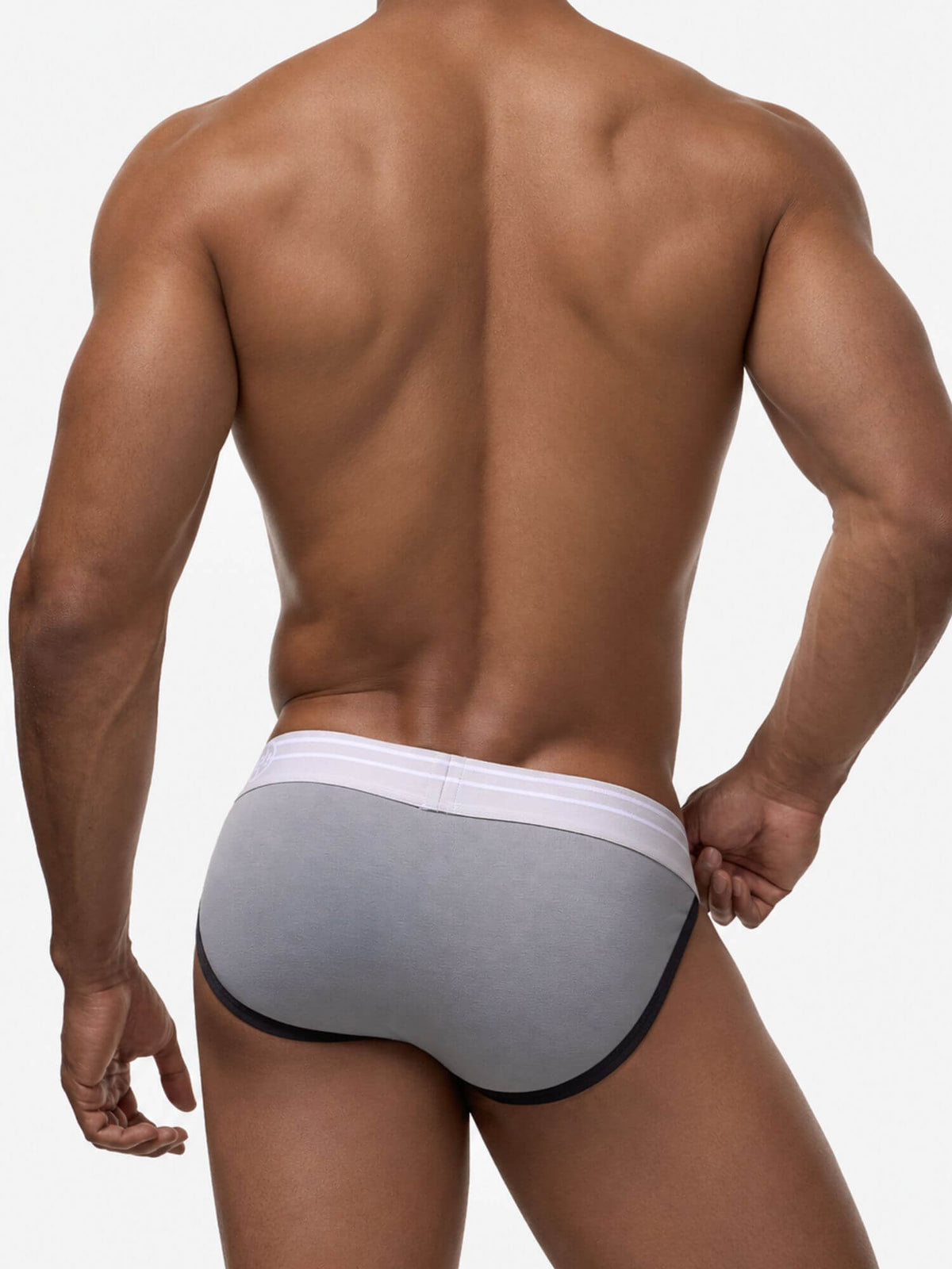 Rear view of a muscular male model wearing a pair of gray briefs with a white waistband and black trim, set against a plain white studio background.
