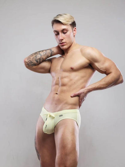 Man wearing light-colored swimwear briefs against a plain background