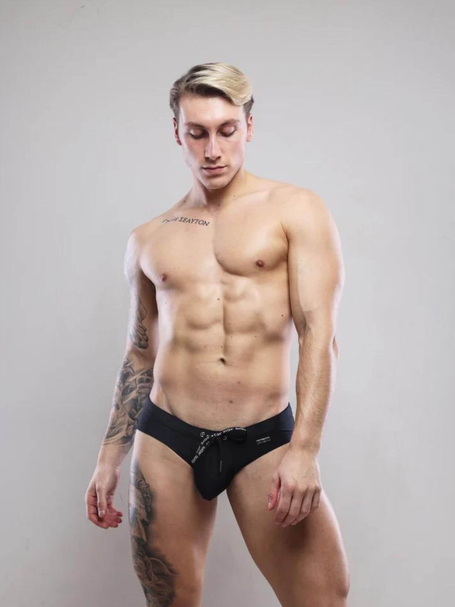 Man wearing black swim briefs against a plain background