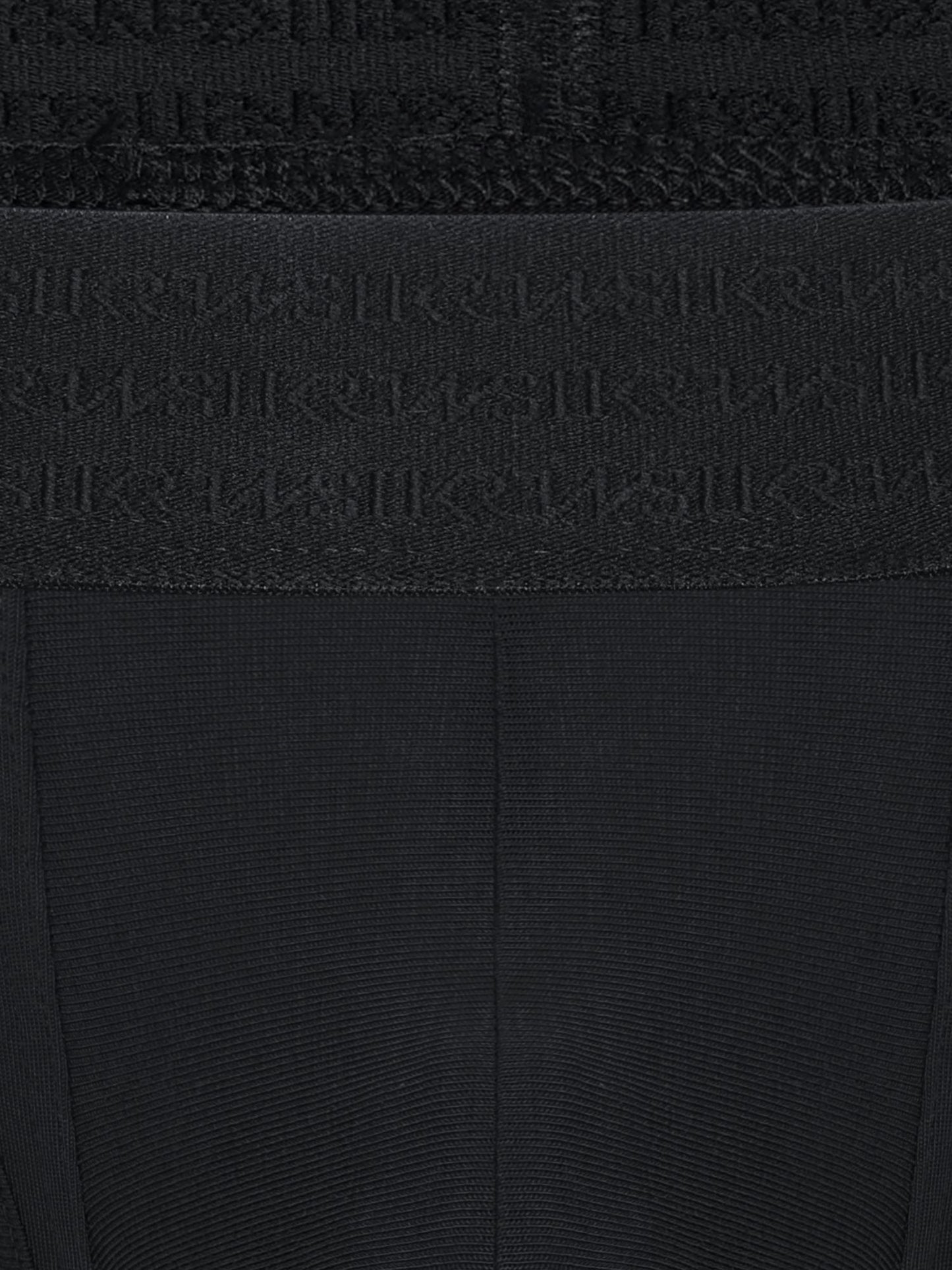 Close-up of a black ribbed knit garment with a wide waistband featuring an embossed repeating SUKREW logo pattern.