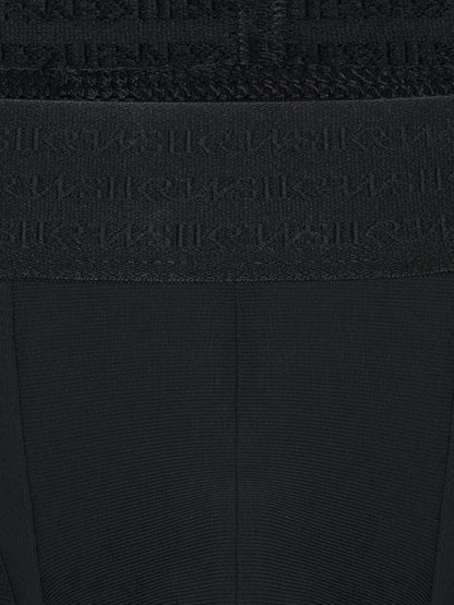Close-up of a black ribbed knit garment with a wide waistband featuring an embossed repeating SUKREW logo pattern.
