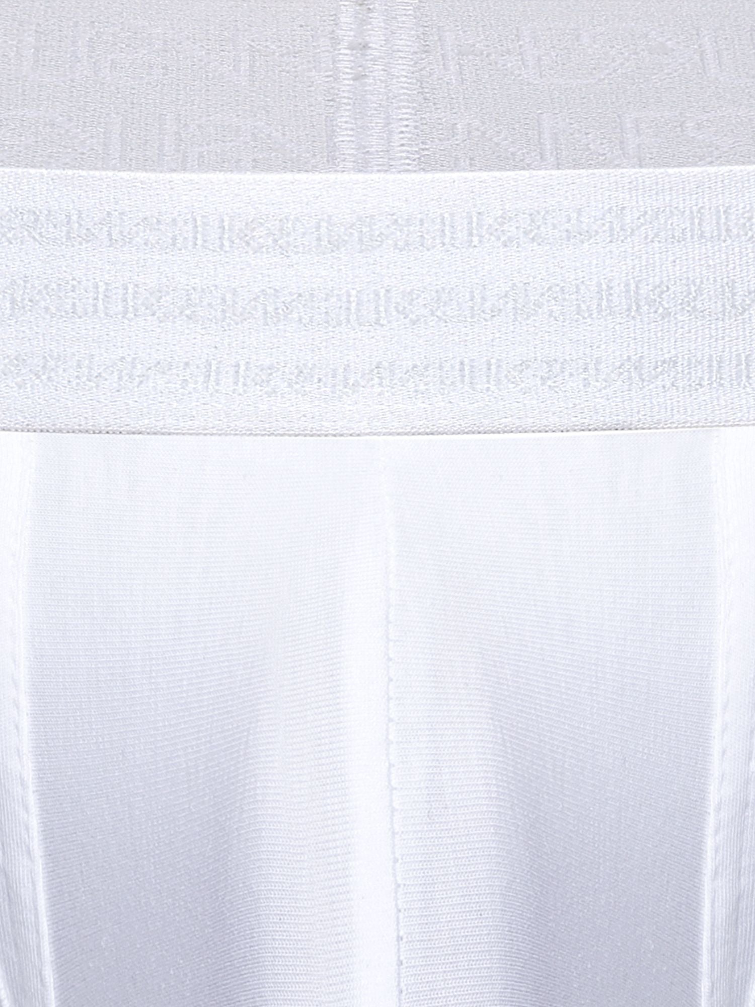 Close-up of a white underwear or garment waistband with a repeating tonal SUKREW logo pattern, shown against matching white fabric.