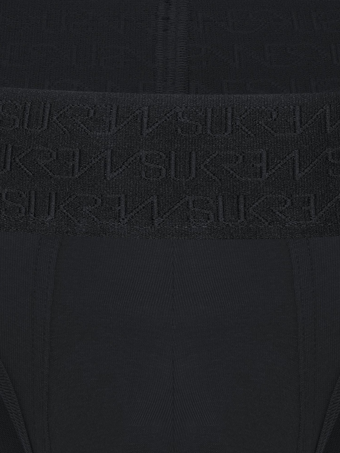 Close-up of a black ribbed knit garment with a wide waistband featuring an embossed repeating SUKREW logo pattern.