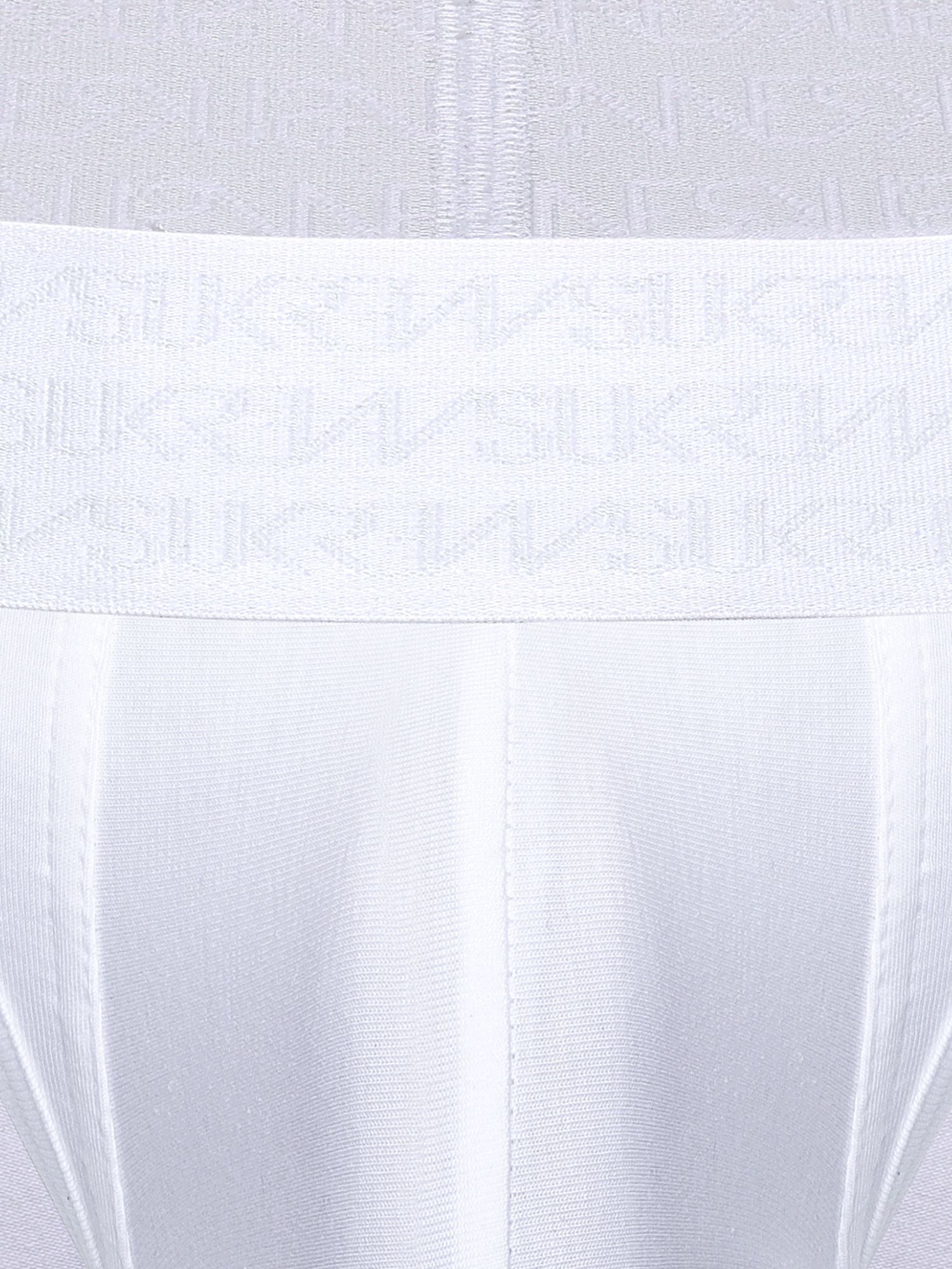 Close-up of a white underwear or garment waistband with a repeating tonal SUKREW logo pattern, shown against matching white fabric.