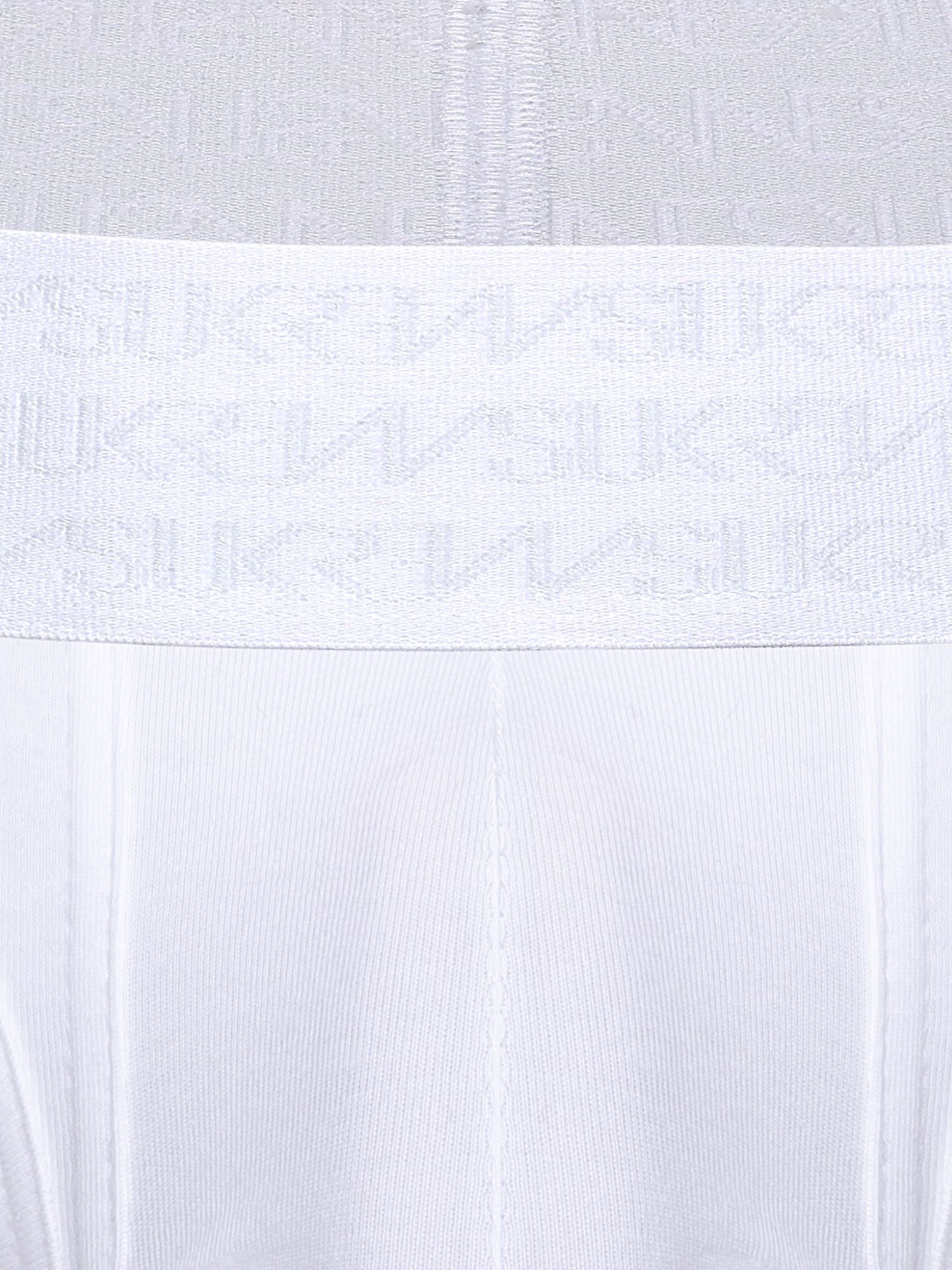 Close-up of a white underwear or garment waistband with a repeating tonal SUKREW logo pattern, shown against matching white fabric.