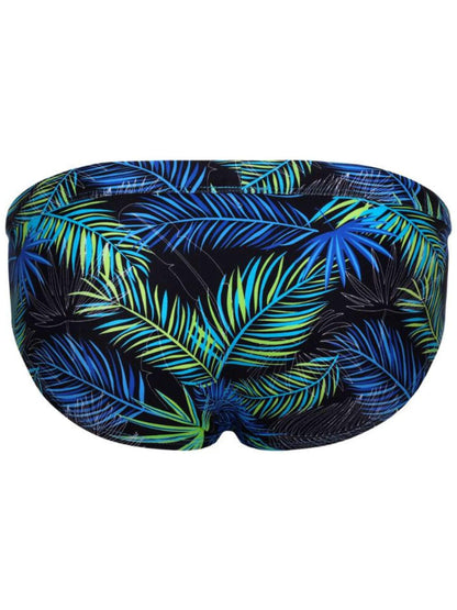 A swim brief featuring a vibrant tropical palm leaf pattern in shades of blue, green, and yellow on a black background, shown against a plain white backdrop.