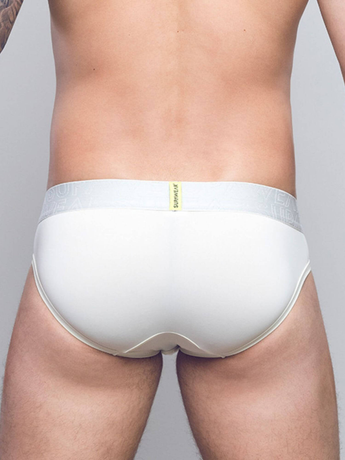 Rear view of a man wearing white briefs with a light gray elastic waistband and a small yellow brand tab.