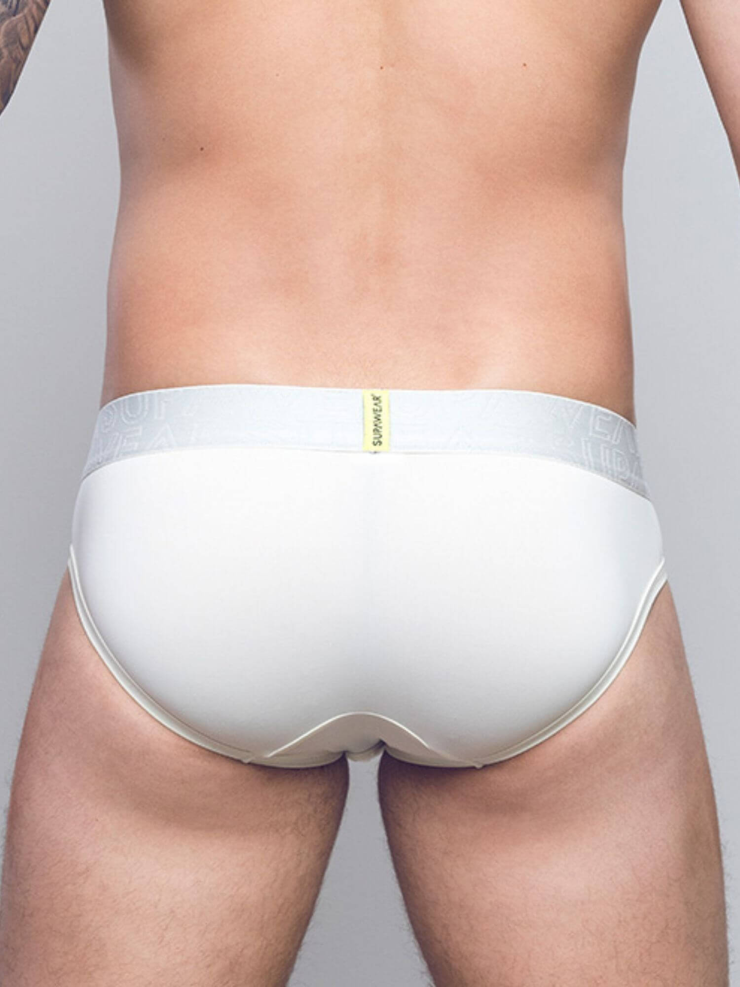 Rear view of a man wearing white briefs with a light gray elastic waistband and a small yellow brand tab.