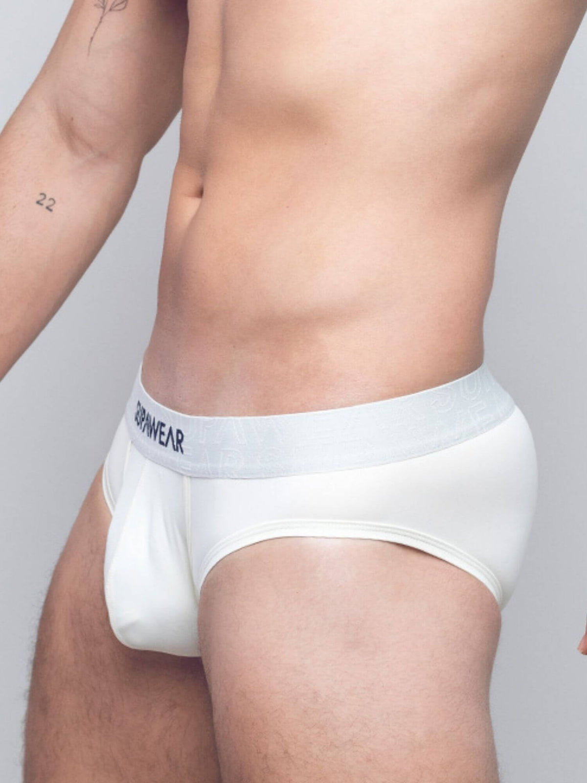 A close-up of a man's lower torso wearing white briefs with a light gray elastic waistband featuring the brand name in black text.