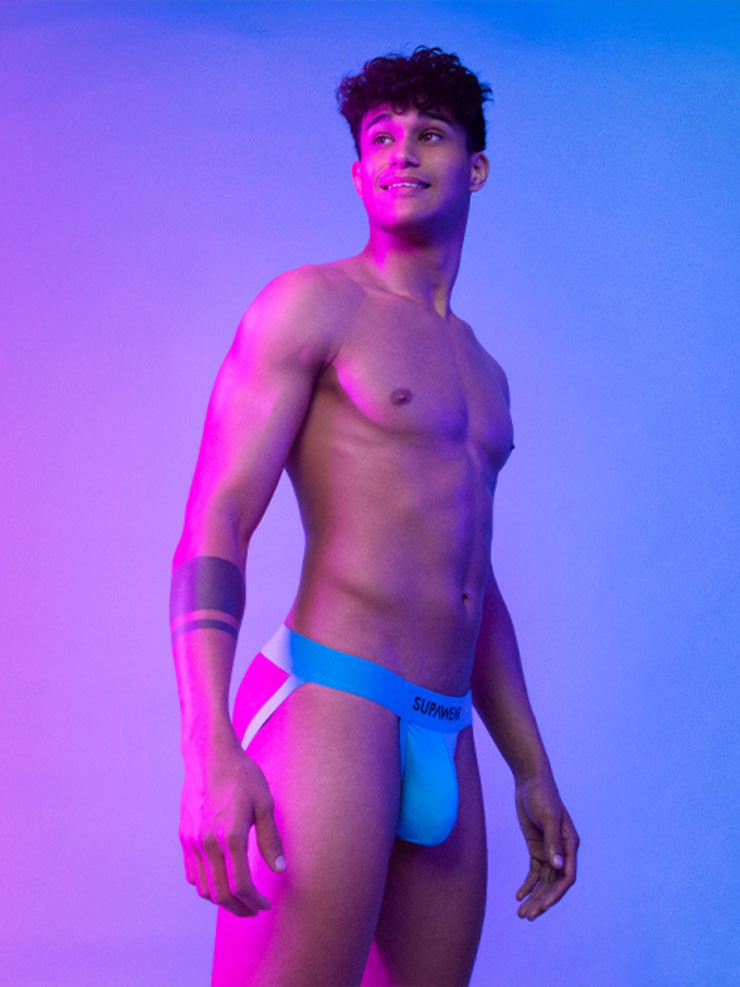 Man wearing blue jockstrap against a gradient purple and pink background