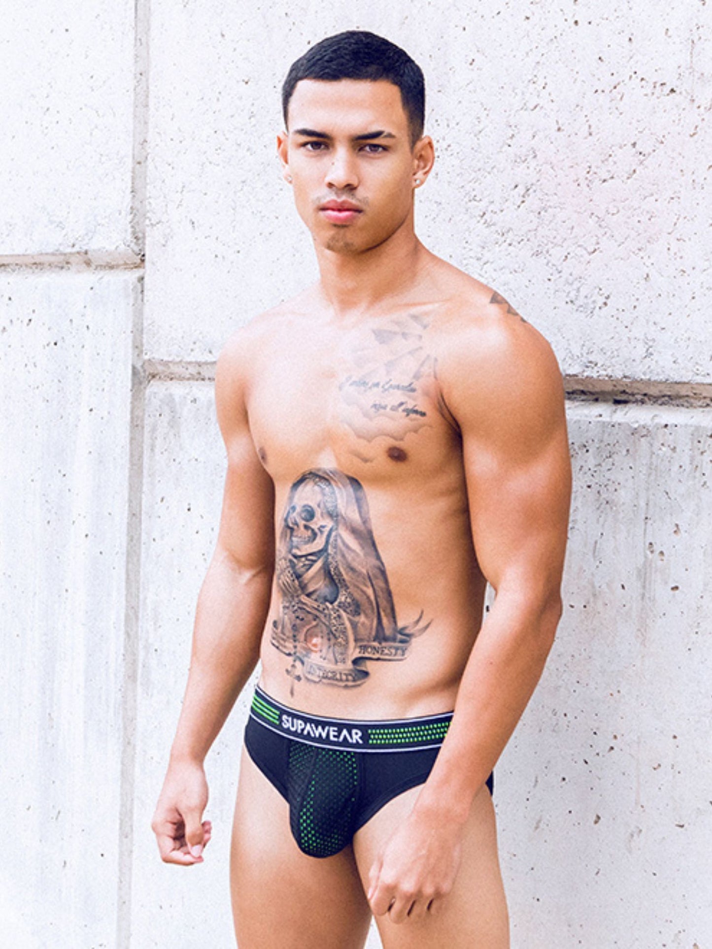 Man wearing black underwear with visible branding against a light-colored wall.