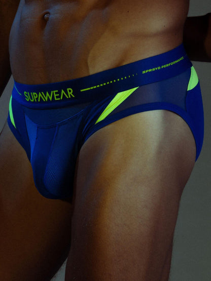 Close-up of a man wearing blue and neon yellow athletic briefs with the brand name SUPAWEAR visible on the waistband.