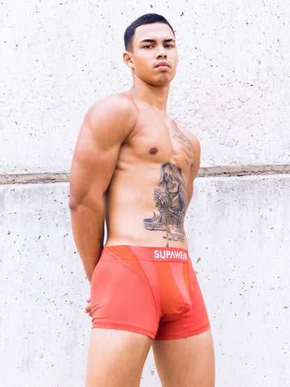 Man wearing red underwear with 'Supawear' brand logo against a textured wall.