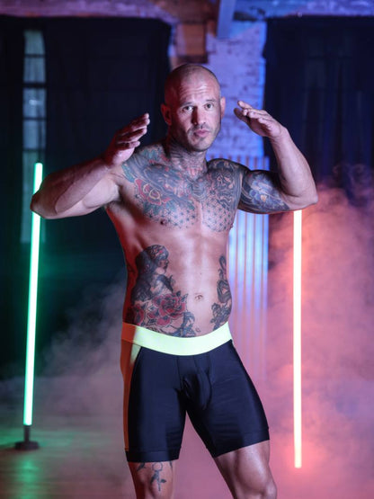 Man with tattoos posing in a dark room with neon lights
