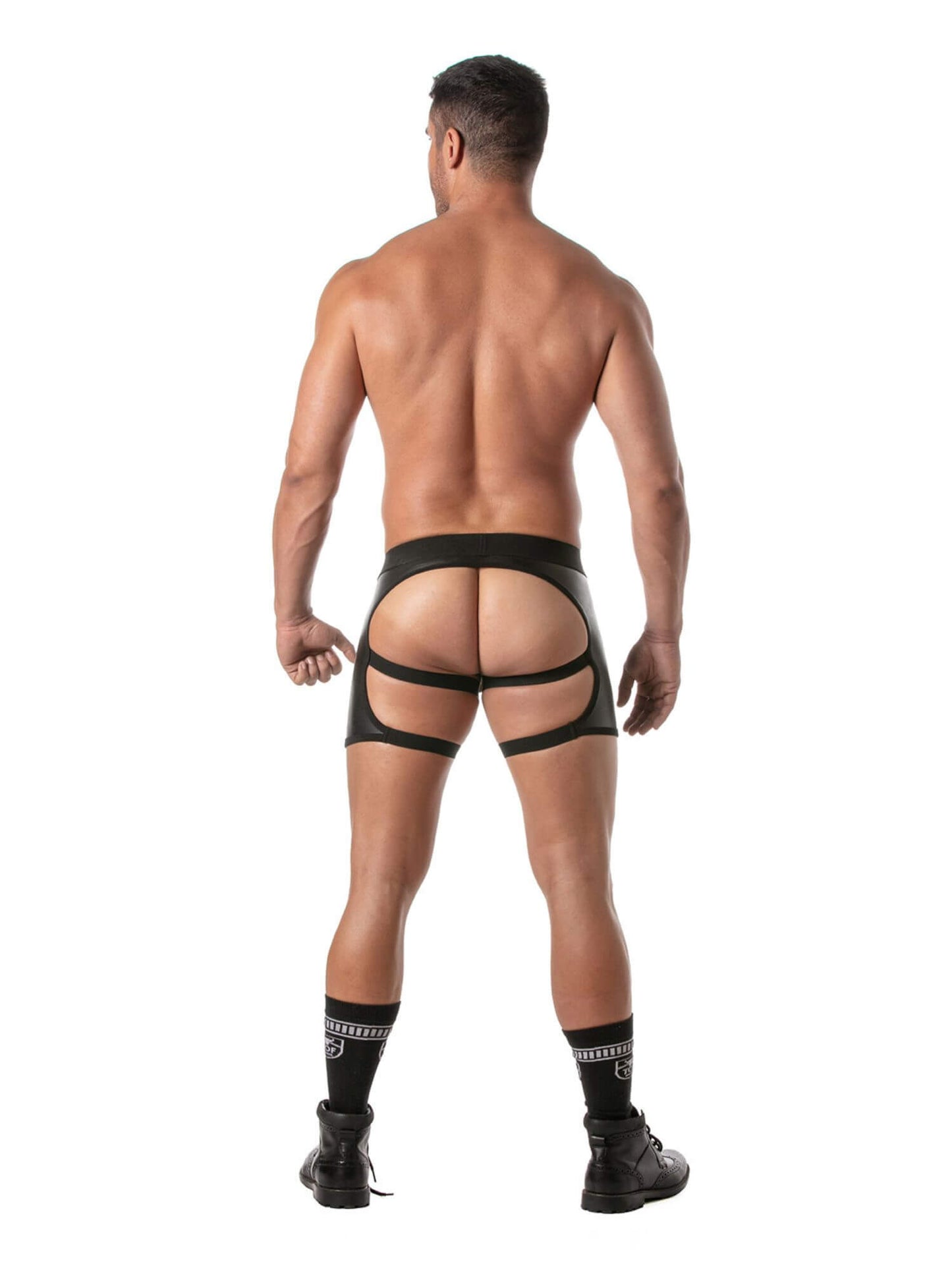 Rear view of a shirtless man wearing black strappy adult underwear with a wide waistband and leg straps, standing against a plain white background.