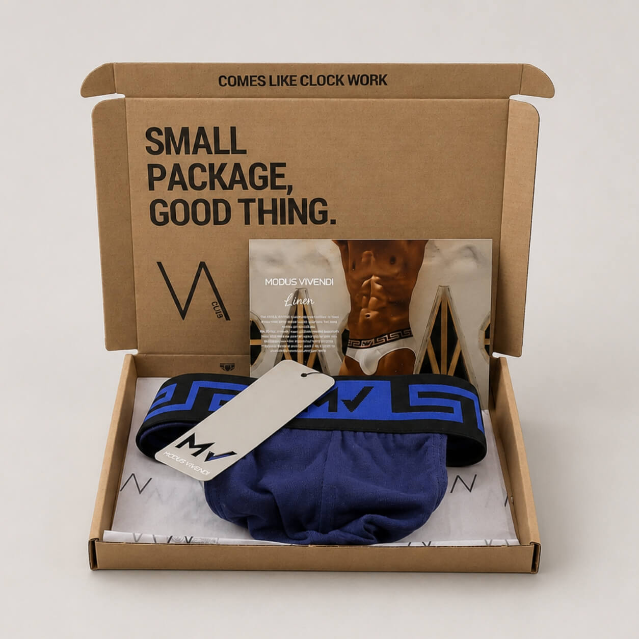 An example of a VA CLUB subscription box on a light grey background containing a MODUS VIVENDI navy blue cotton thong wih the Greek key design on the waistband, a brand tag, VOCLA branded tissue paper and a small printed product insert card