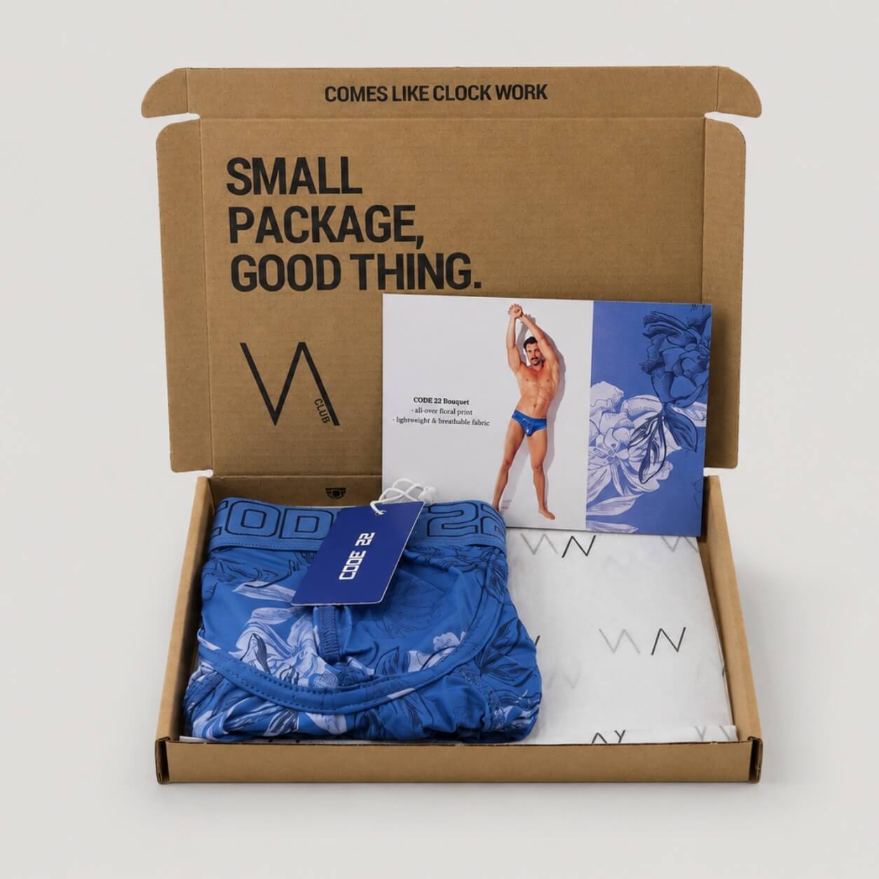 An example of a VA CLUB subscription box on a light grey background containing a CODE 22 Bouquet blue floral print boxer brief with CODE 22 brand tag, VOCLA branded tissue paper and a small printed product insert card
