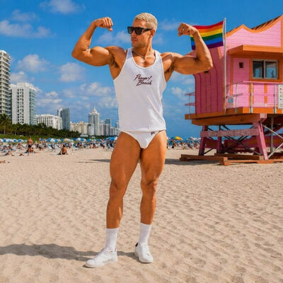 A muscular man posing on a sunny beach wearing a white tank top with 'PUMP Beach' printed on the chest, white swimming briefs, white socks, and white sneakers. A pink lifeguard tower and a rainbow flag are visible in the background. The outfit is part of the VOCLA men's beachwear collection