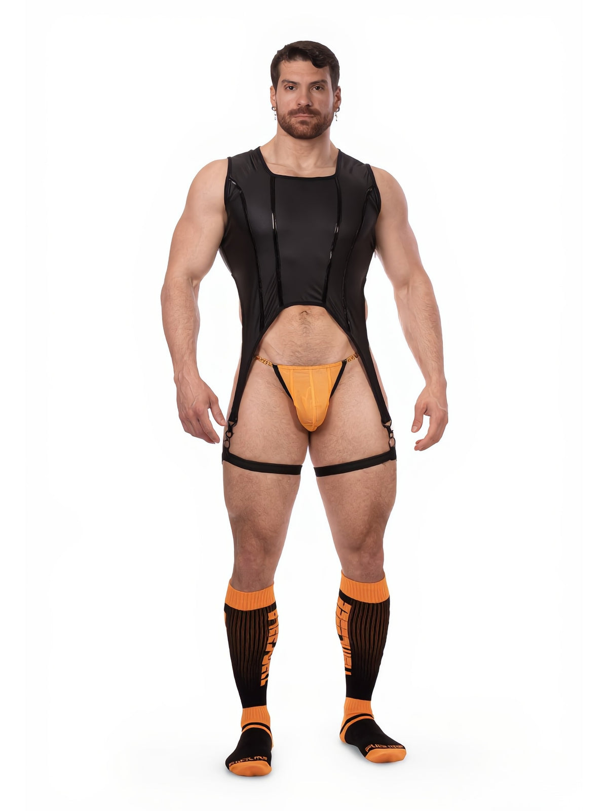 A muscular man modeling a black strappy rocky horror show bodysuit harness with an orange thong and matching orange and black compression socks, set against a plain white background.