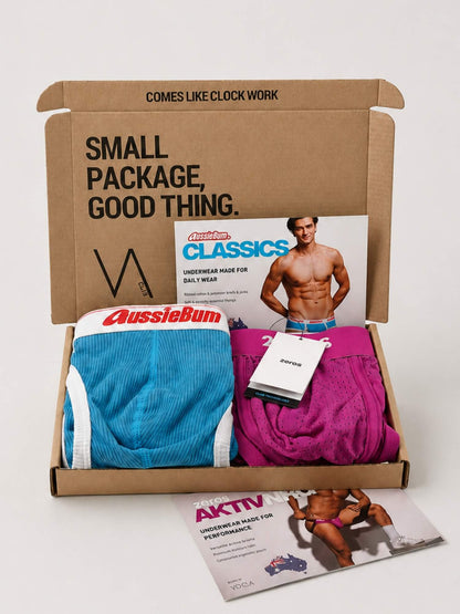 An open cardboard VA CLUB subscription box from AussieBum containing underwear, a magazine insert, and a small booklet, photographed on a clean light background.