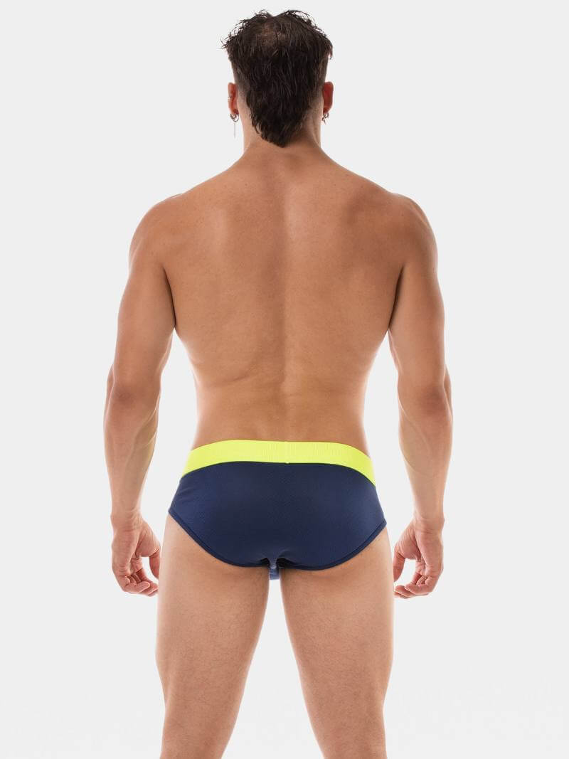 Man wearing navy swim briefs with a yellow waistband on a white background