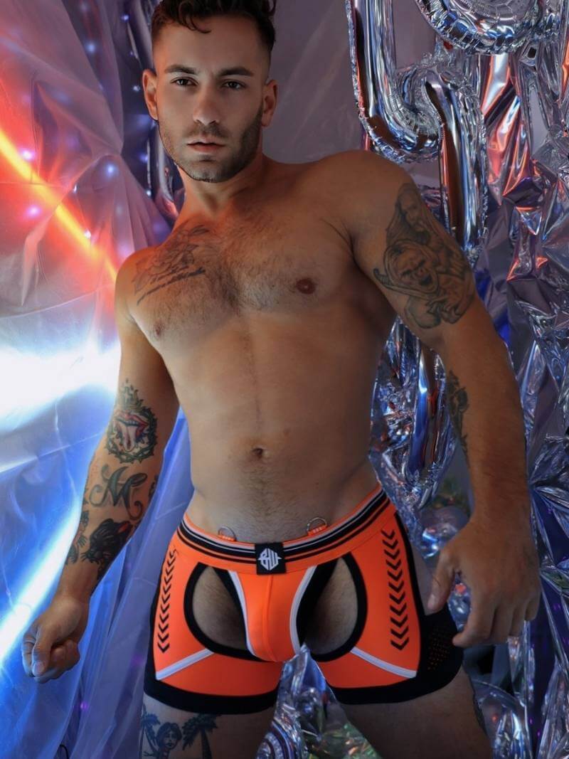 Man wearing bright orange and black underwear with a colorful, reflective background