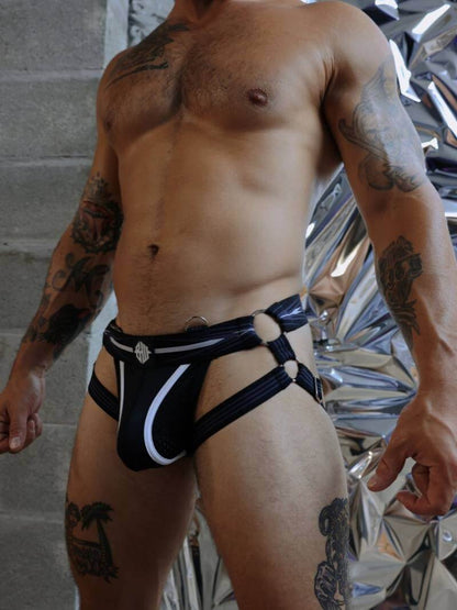 Man wearing a black and white thong with tattoos visible on arms and legs.