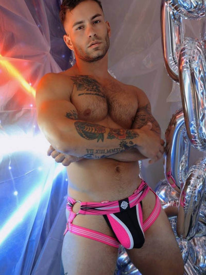 Man wearing a pink and black jockstrap with tattoos on a colorful background