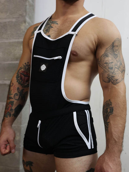 Person wearing a black overalls with white trim and suspenders against a neutral background