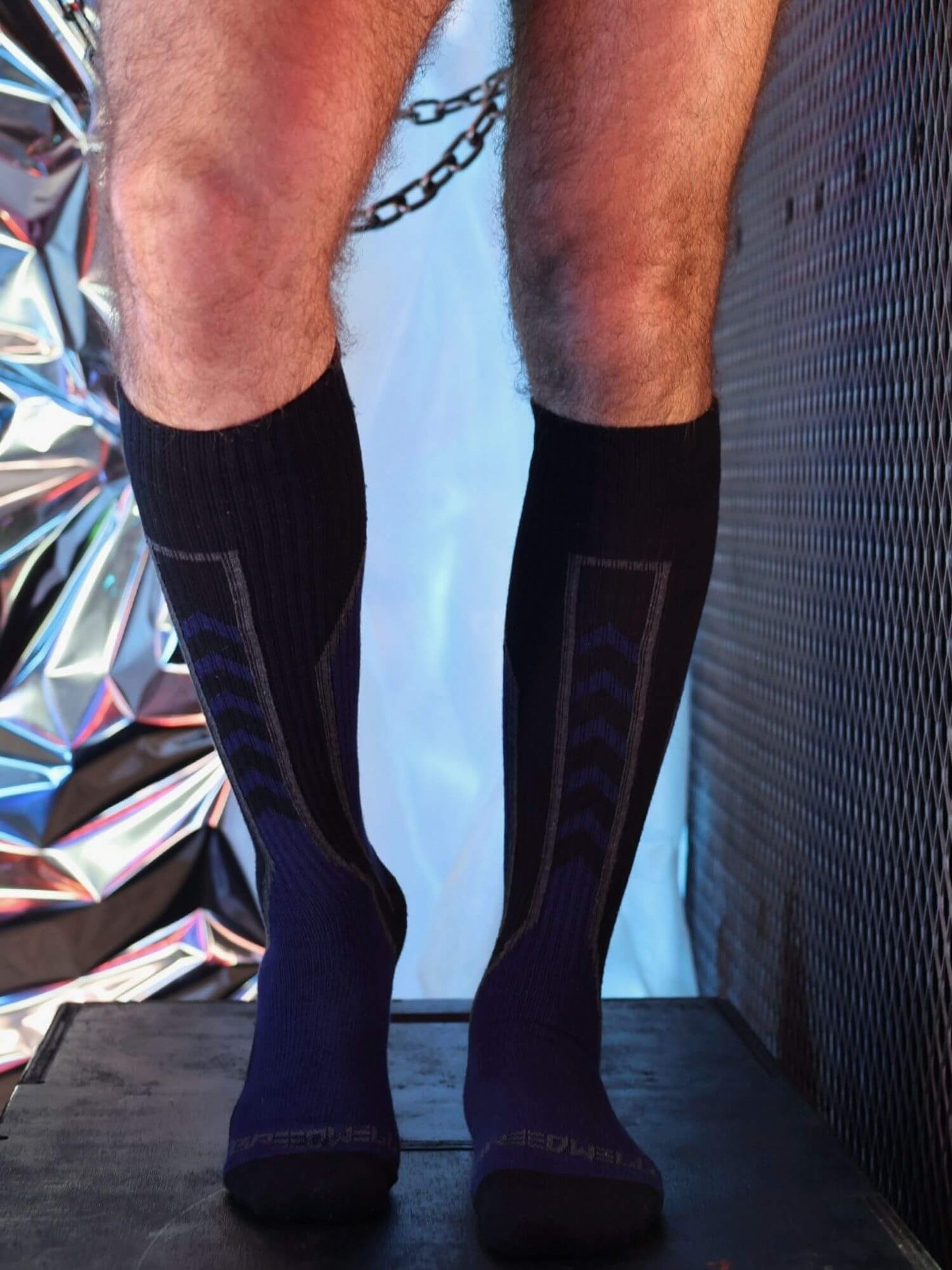 Person wearing black knee-high socks with a patterned design against a reflective surface.