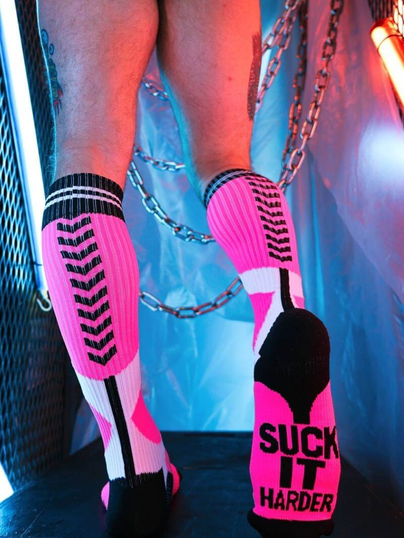 Person wearing pink and black socks with text, standing in a colorful, abstract setting.
