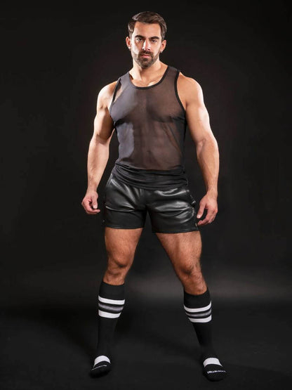 Man wearing a black tank top and shorts with striped socks on a black background