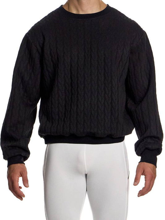 Person wearing a black cable knit sweater and white pants on a white background
