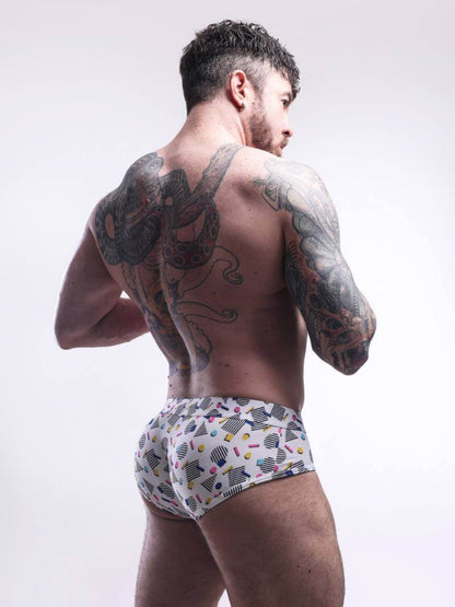 Man wearing patterned underwear with tattoos on his back and arms against a white background
