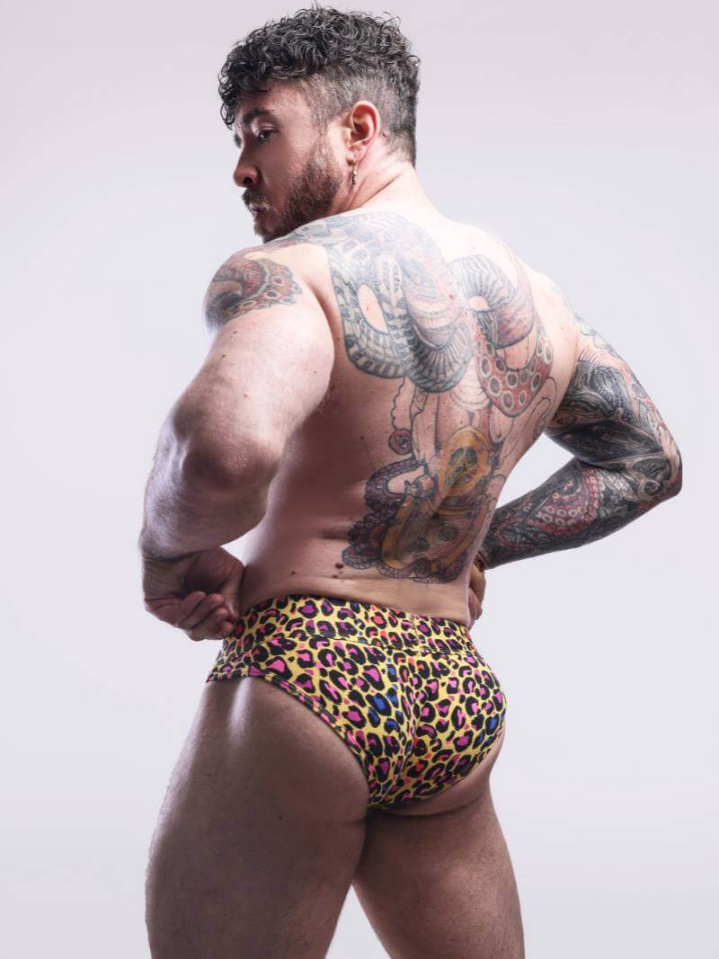 Man wearing colorful leopard print underwear with tattoos on a plain background