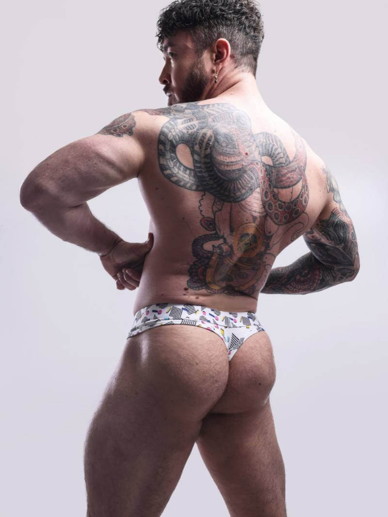 Man with tattoos on his back wearing a patterned underwear against a plain background