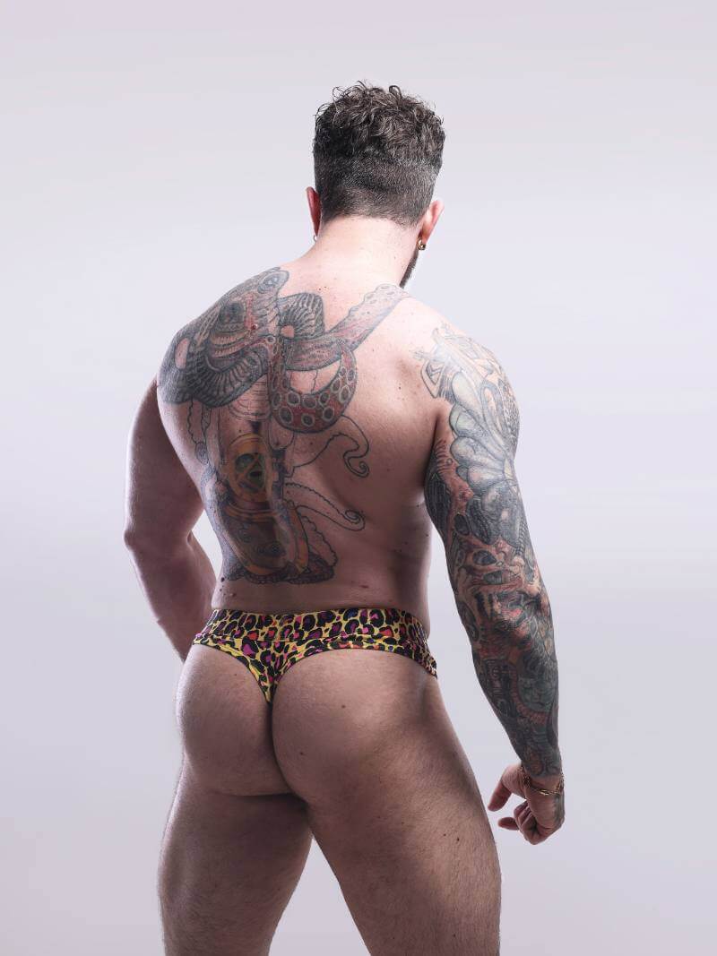 Man with tattoos wearing leopard print underwear on a plain background