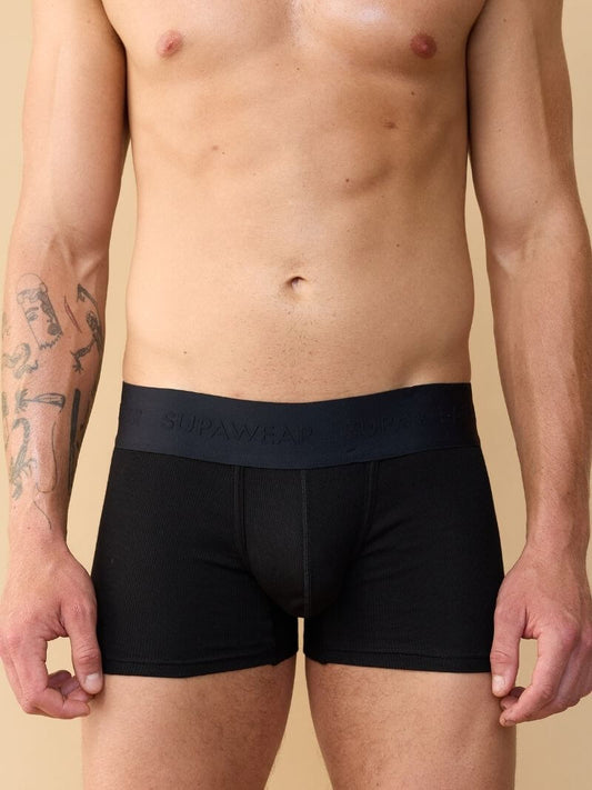 Man wearing black boxer briefs with a visible brand logo on a beige background